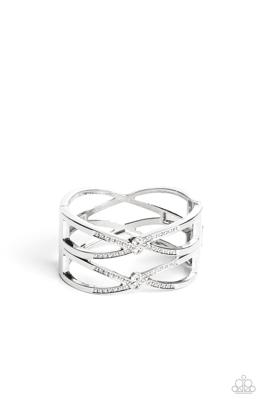 Paparazzi Accessories Entrancing Etiquette - White High-sheen silver bars airily weaves around the wrist in a zig-zag manner into a refined statement. Featured on the crossed ribbons of the silver, rows of dainty white rhinestones cluster across the displ