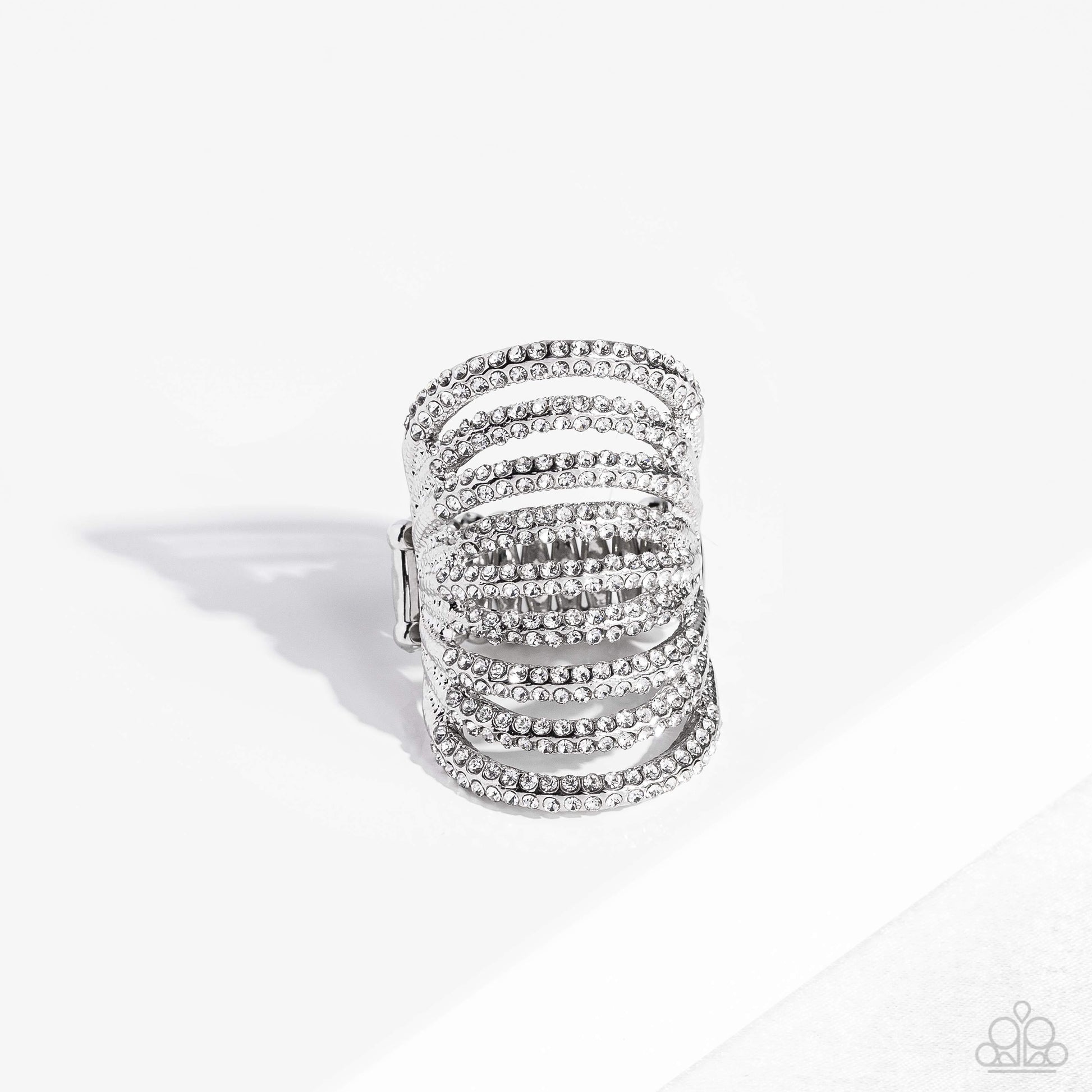 Paparazzi Accessories Rippling Rarity - White An elongated silver frame, lined with dainty white rhinestones, creates the illusion of endless sparkle as it stacks up the finger. Encrusted in two rows across each silver band as it arcs across the finger, t