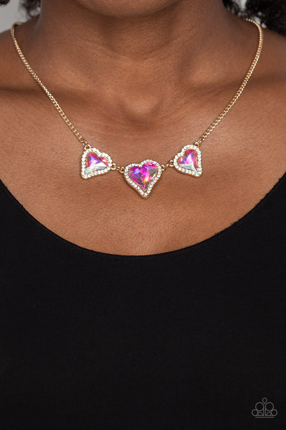 Paparazzi Accessories State of the HEART - Gold Nestled in white rhinestone frames, a trio of glittery iridescent heart-shaped gems delicately links and dangles down the neckline for a dash of swoon-worthy shimmer on a gold chain. Features an adjustable c