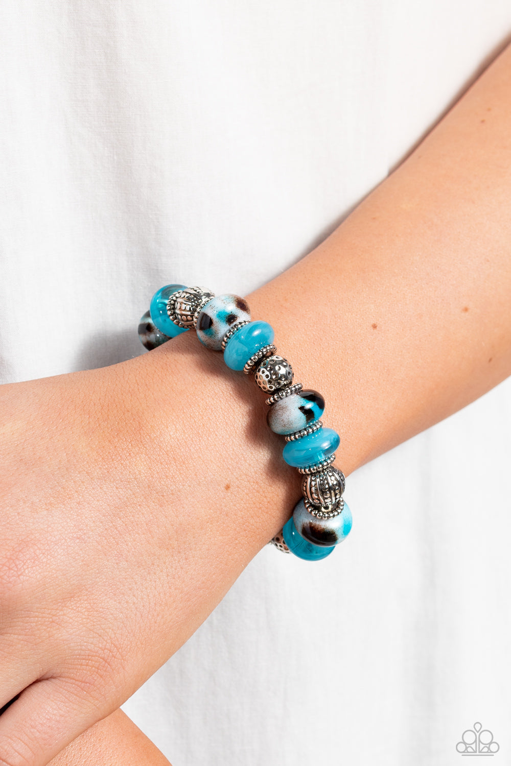 Paparazzi Accessories Warped Wayfarer- Blue An earthy collection of dotted silver beads, rounded milky turquoise beads, studded silver rings, turquoise-spotted ceramic-like beads and textured silver beads are threaded along an elastic stretchy band around