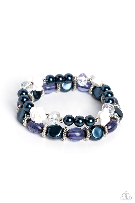 Paparazzi Accessories Who ROSE There? - Blue Montana pearls, silver studded rings, varying shapes of Montana and clear blue beads, silver accents, faceted clear beads, and white resin roses stretch across elastic stretchy bands around the wrist for a refi