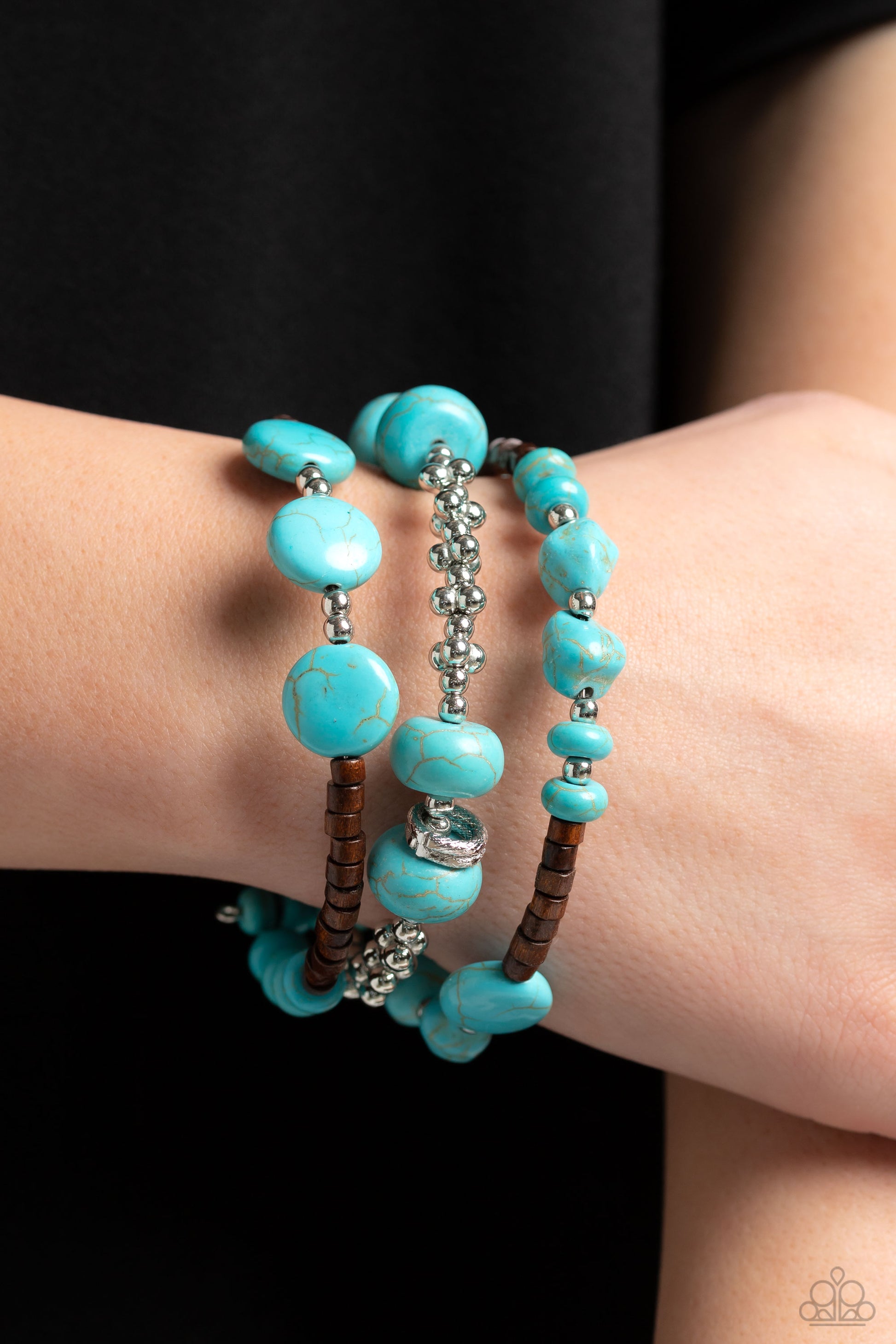 Paparazzi Accessories Operation Outdoors - Blue An earthy collection of brown wooden beads, classic silver beads and accents, and turquoise stones in varying sizes are threaded along invisible wires to create three bands that arc across the wrist. The ban