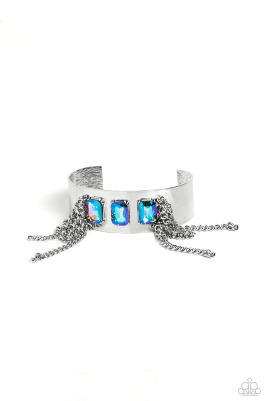 Paparazzi Accessories CHAIN Showers - Multi A thick, industrial silver cuff is topped by three brilliant UV-shimmery, emerald-cut gems. Strands of silver curb chain stream from each side of the trio of glitz, adding undeniable drama and eye-catching movem