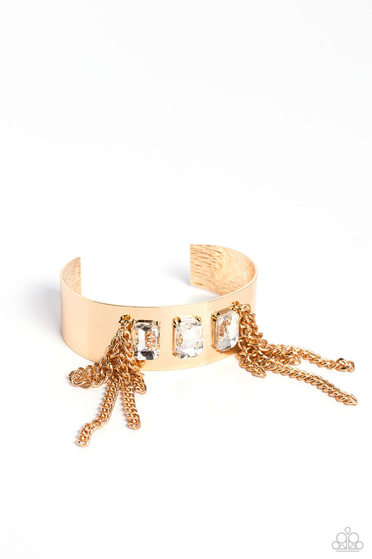 Paparazzi Accessories CHAIN Showers - Gold A thick, industrial gold cuff is topped by three brilliant white, emerald-cut gems. Strands of gold curb chain stream from each side of the trio of glitz, adding undeniable drama and eye-catching movement to the