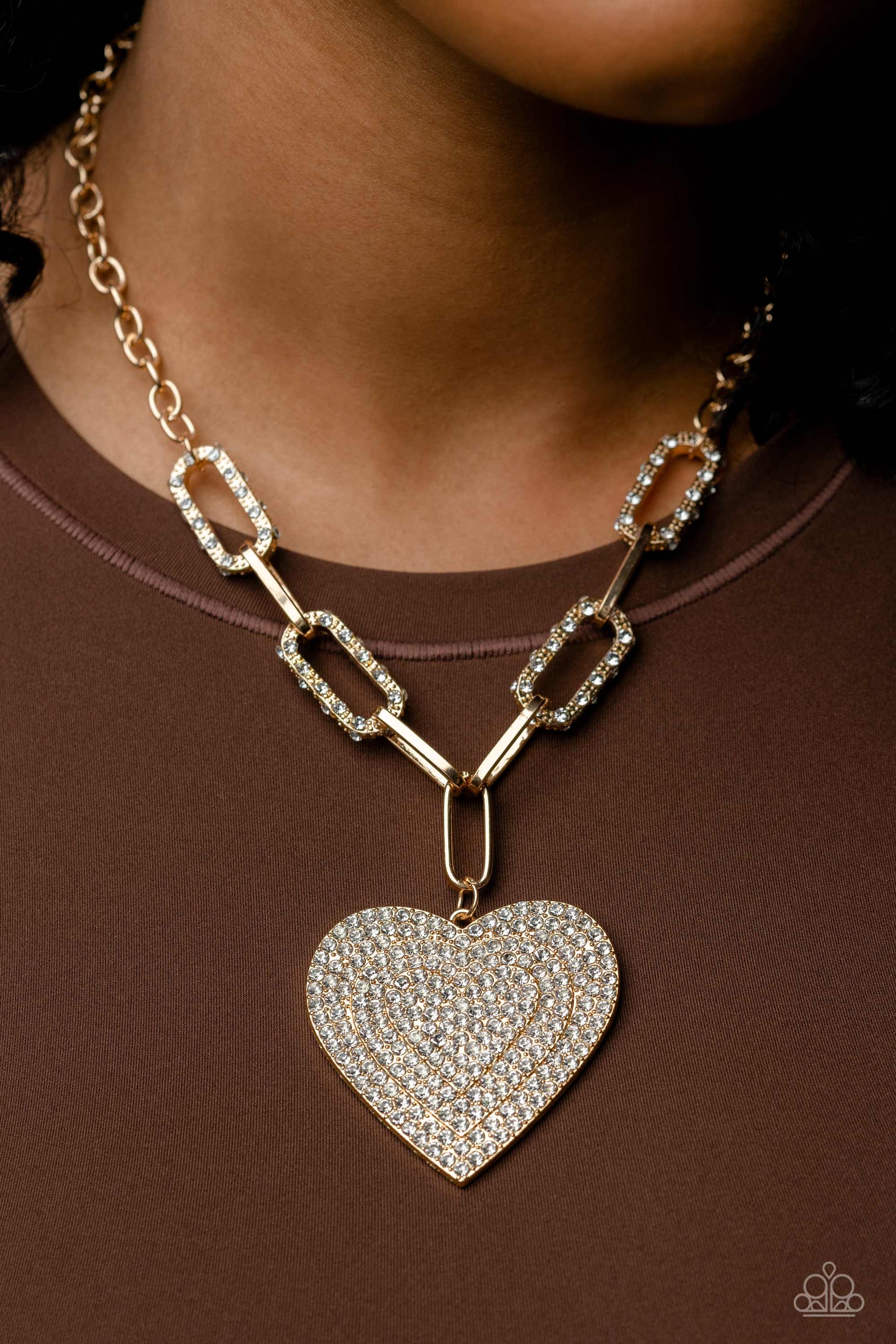 Paparazzi Accessories Roadside Romance - Gold Elongated, oversized gold links, encrusted with a blinding display of white rhinestones and shimmery gold accents connect a classic gold chain to an exaggerated gold heart pendant for a romantically refined fi
