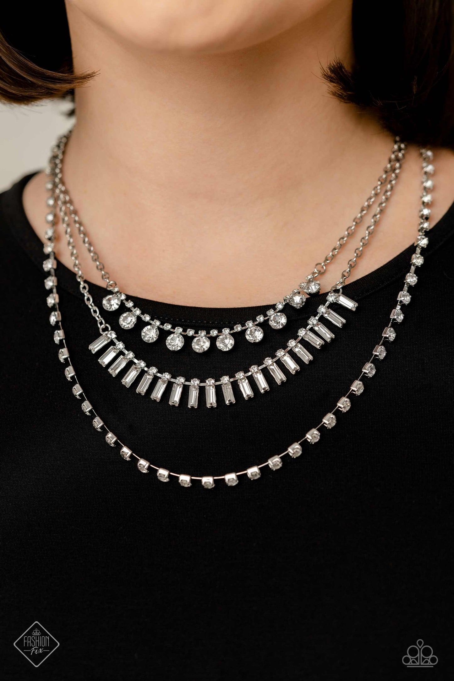 Paparazzi Accessories Dripping in Stardust - White Three silver chains fall into haphazard layers across the chest, creating a radiantly edgy display. On the uppermost chain, a row of solitaire rhinestones emerges from a section of small, white, square-cu