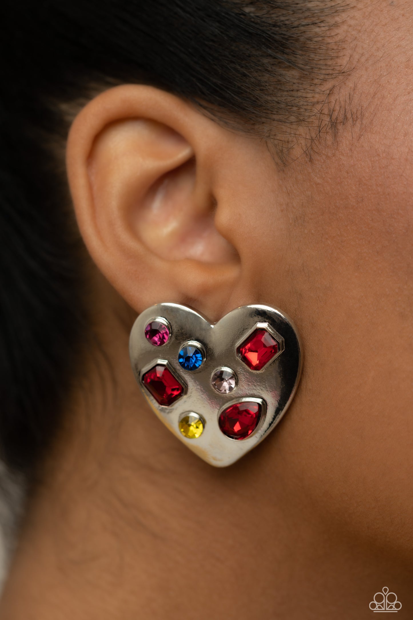 Paparazzi Accessories Relationship Ready - Red Brushed with shimmery pink, yellow, blue, and red round, teardrop and emerald-cut gems, an oversized, high-sheen silver heart frame rests against the ear for a dazzling finish. Earring attaches to a standard