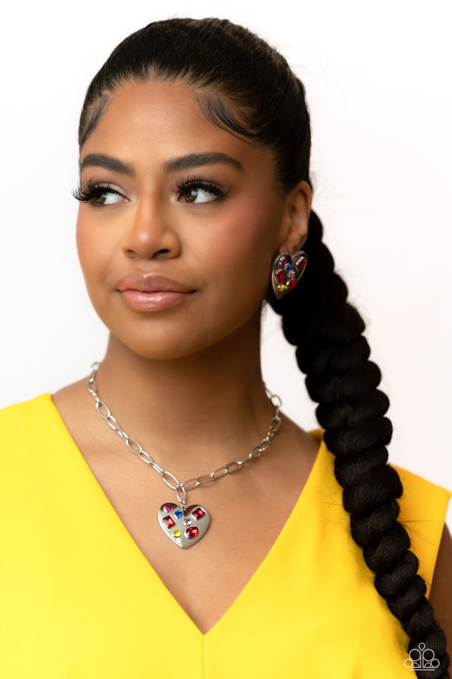 Paparazzi Accessories Relationship Ready - Red Brushed with shimmery pink, yellow, blue, and red round, teardrop and emerald-cut gems, an oversized, high-sheen silver heart frame rests against the ear for a dazzling finish. Earring attaches to a standard