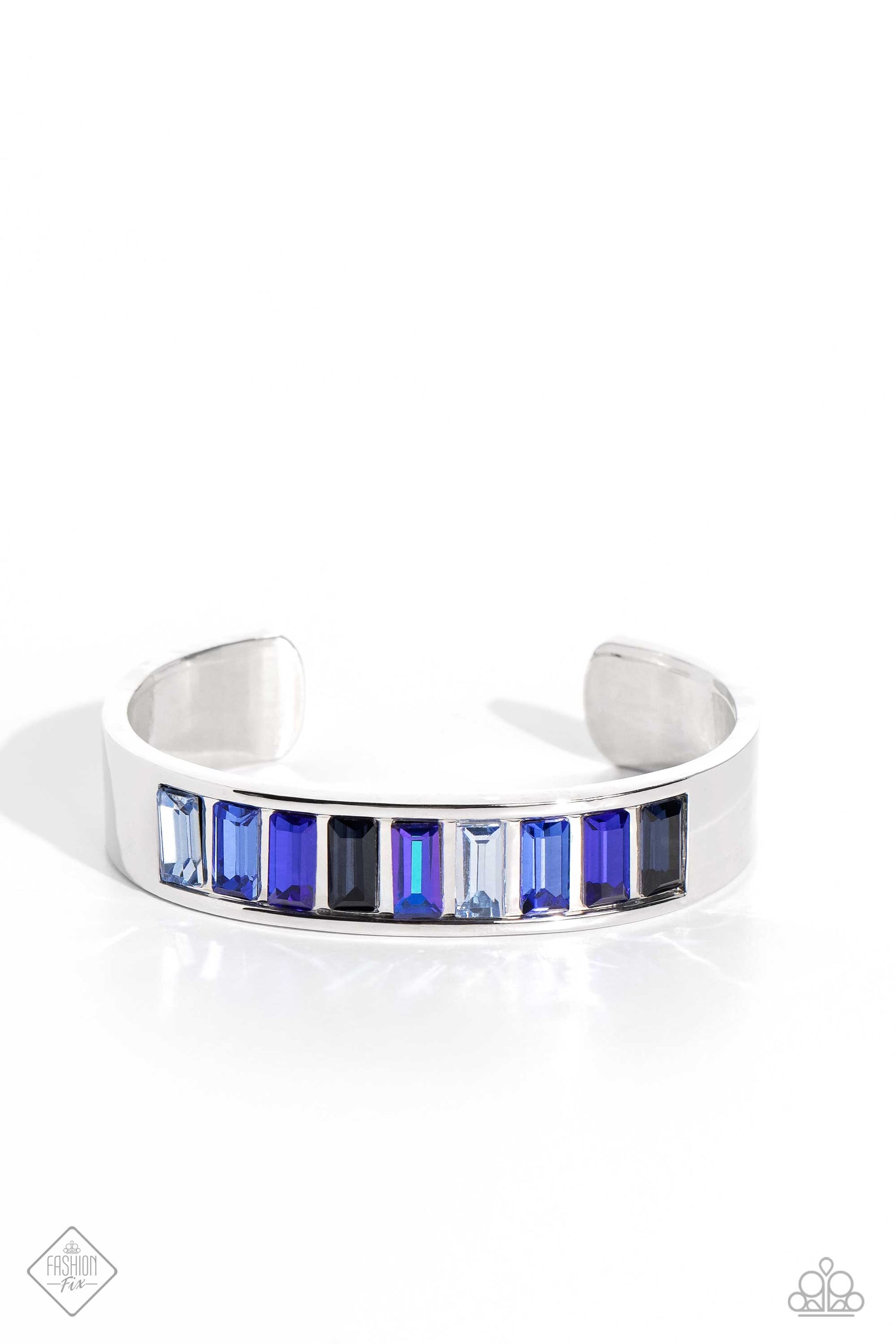 Paparazzi Accessories Practiced Poise - Blue Embedded in the center of a thick, high-sheen silver cuff, a row of glassy emerald-cut gems in varying shades of blue radiates atop the wrist, creating an unexpected pop of color. Sold as one individual bracele