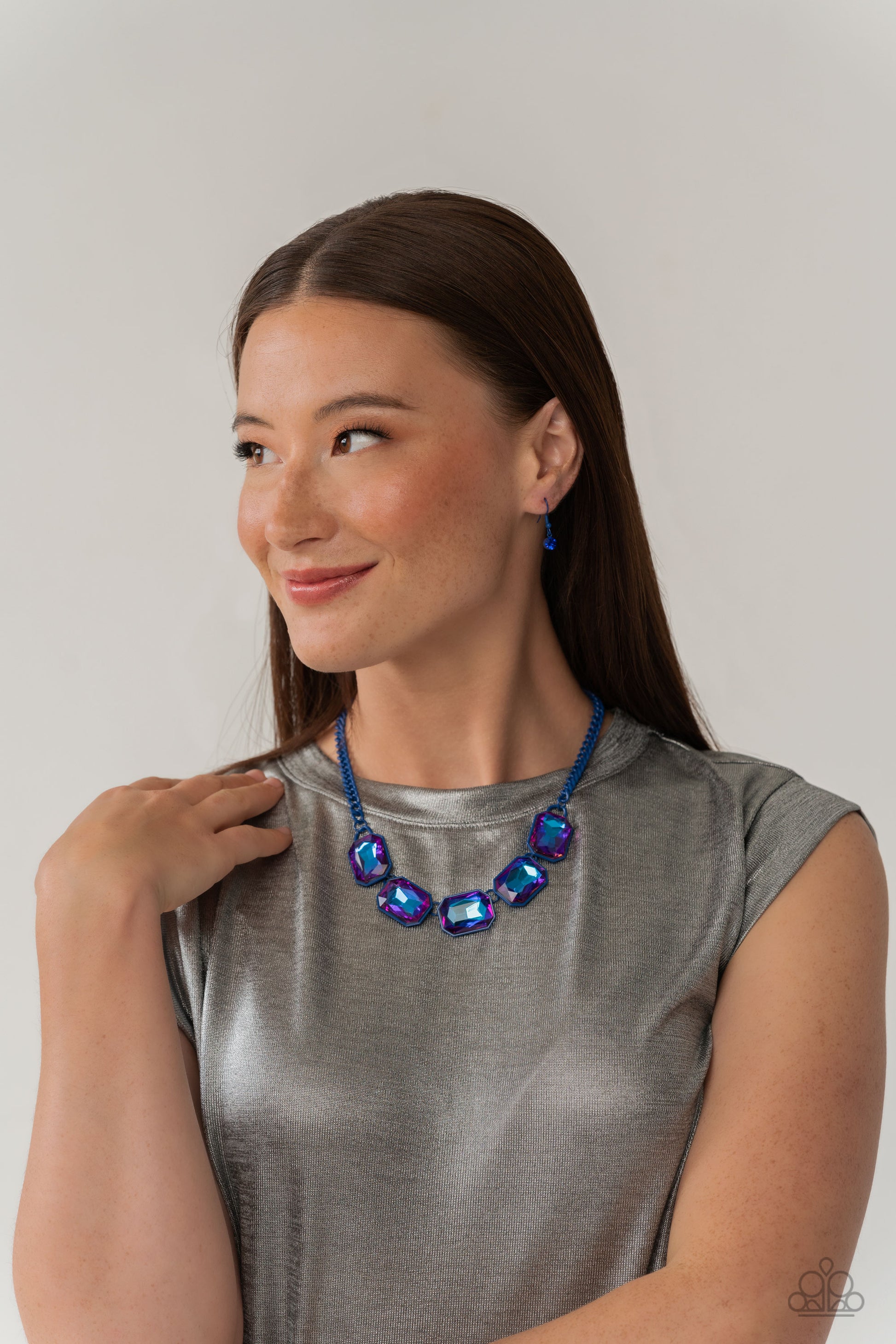 Paparazzi Accessories Emerald City Couture - Blue Featuring a vivacious blue chain, a collection of purple UV shimmery emerald-cut gems, pressed in vibrant blue frames, coalesces around the collar to create a playful pop of edgy color. Features an adjusta