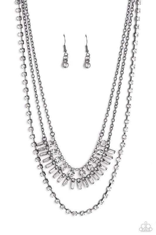 Paparazzi Accessories Dripping in Stardust - Black Three gunmetal chains fall into haphazard layers across the chest, creating a radiantly edgy display. On the uppermost chain, a row of solitaire rhinestones emerges from a section of small, white, square-