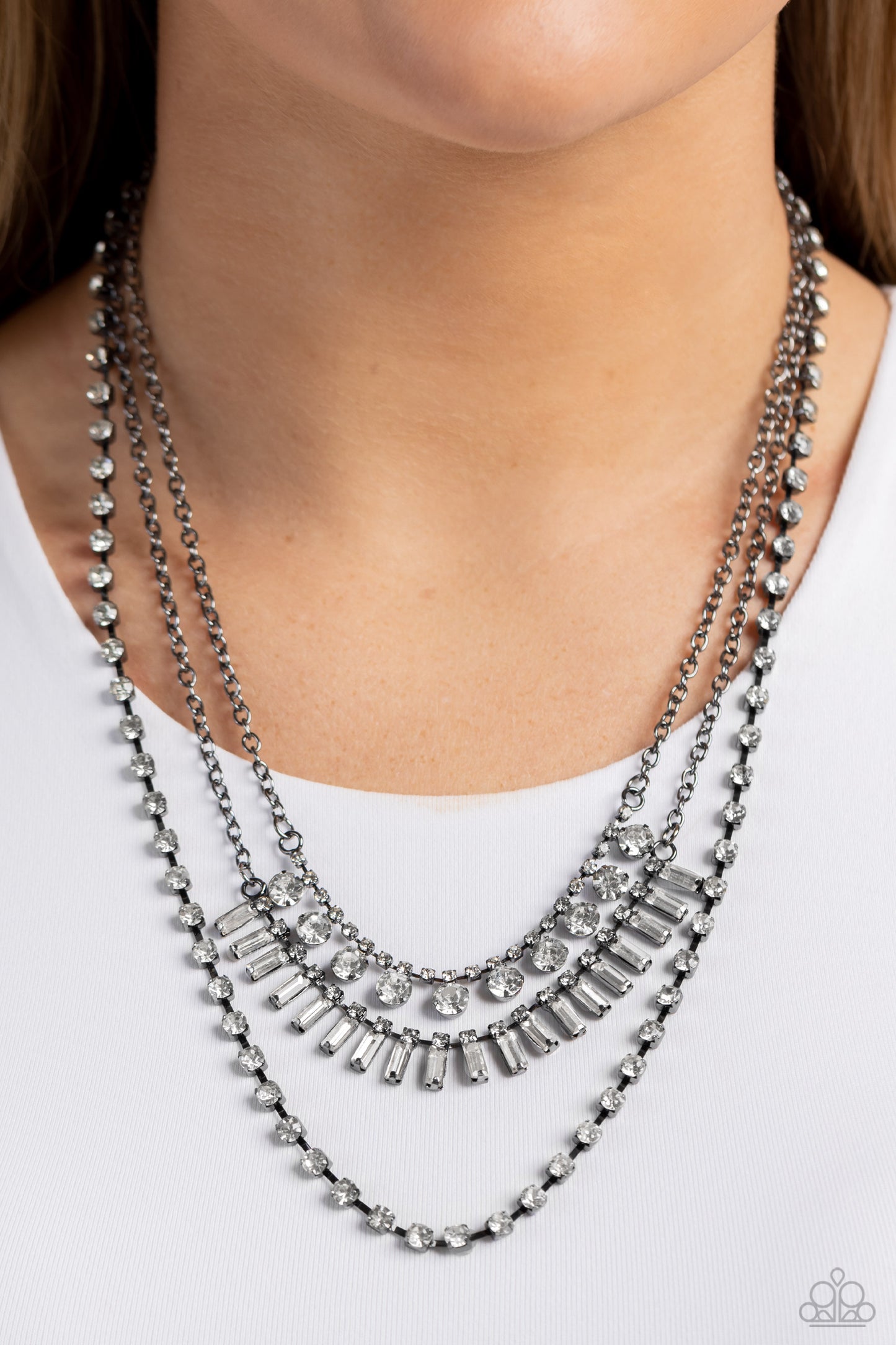Paparazzi Accessories Dripping in Stardust - Black Three gunmetal chains fall into haphazard layers across the chest, creating a radiantly edgy display. On the uppermost chain, a row of solitaire rhinestones emerges from a section of small, white, square-