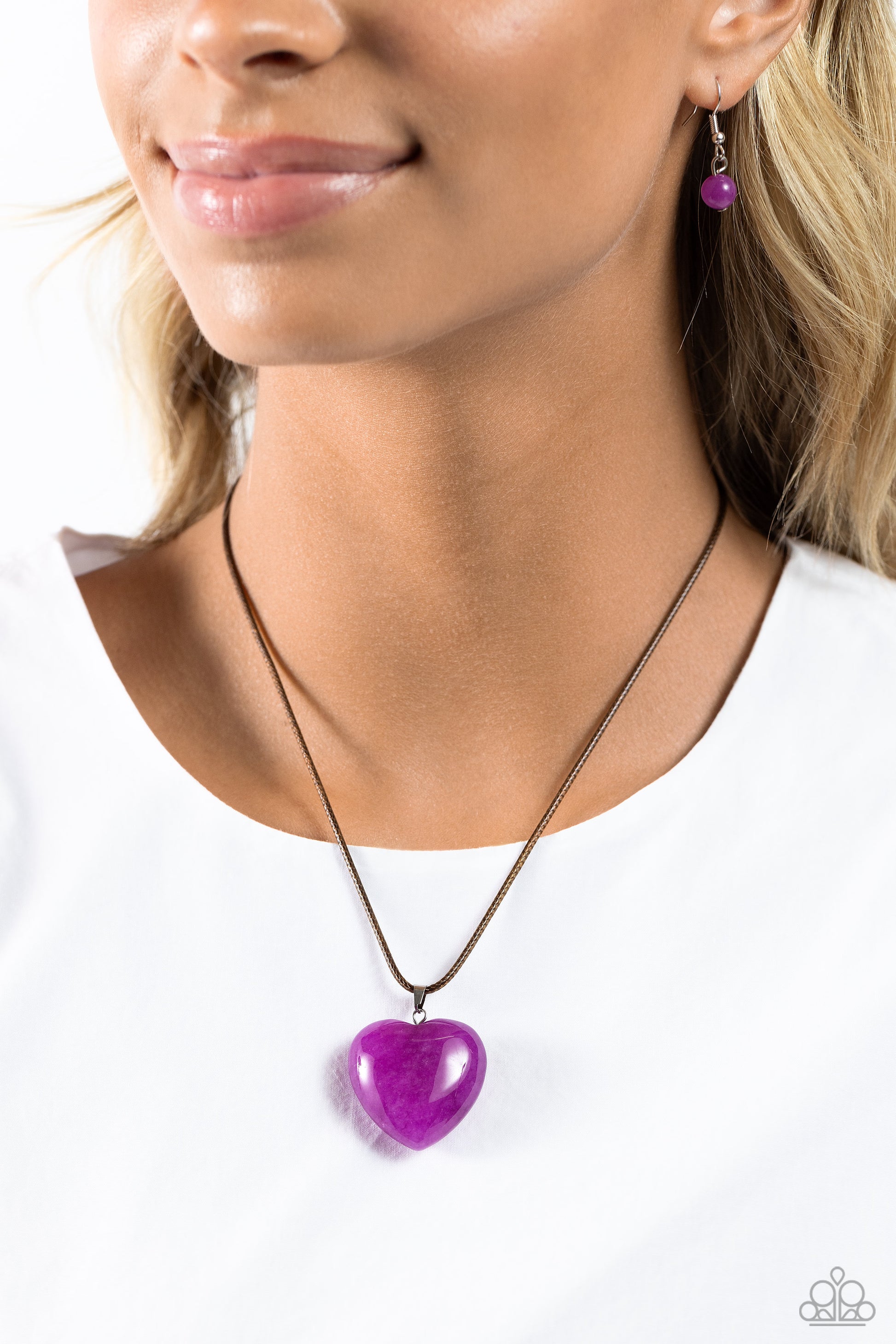 Paparazzi Accessories Serene Sweetheart - Purple Dangling from the bottom of a brown cord, an oversized, amethyst heart glides down the neckline for an earthy serene statement. Features an adjustable clasp closure. As the stone elements in this piece are