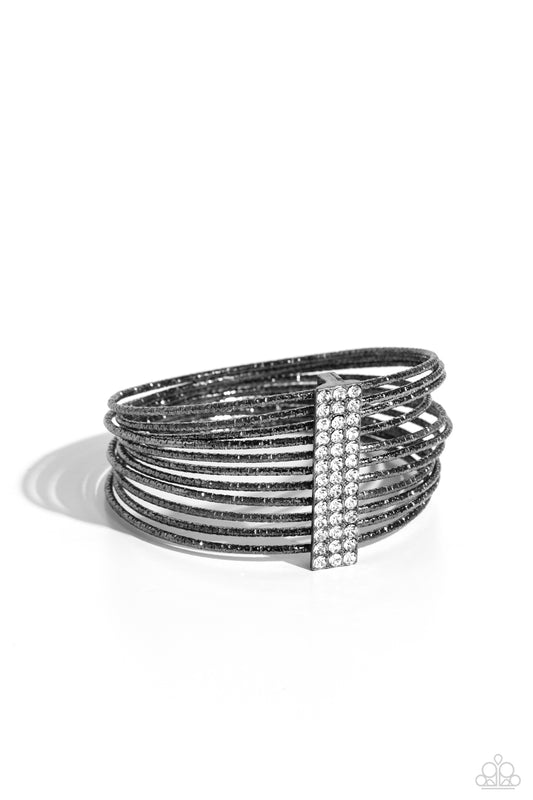 Paparazzi Accessories Shimmery Silhouette - Black Held together by an elongated rectangular gunmetal fitting and encrusted in three rows of white gems, gunmetal bangles embossed in shimmery diamond-cut textures stack across the wrist for a refined display