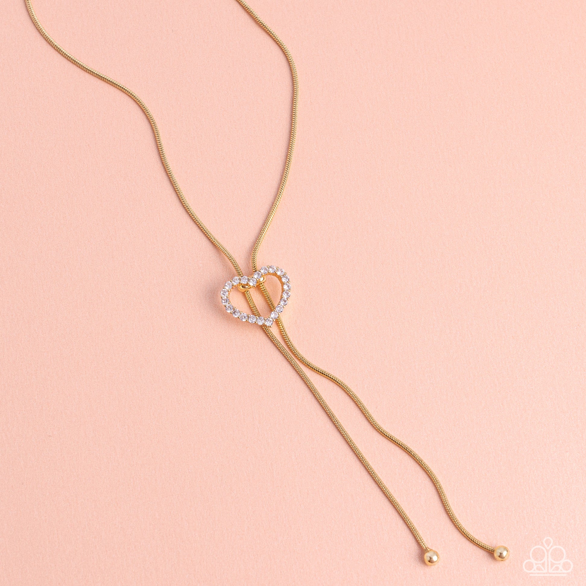 Paparazzi Accessories Tempting Tassel - Gold A dainty white rhinestone-encrusted heart silhouette slides along dainty strands of glistening gold snake chain for a timeless, refined tassel. Features a bolo closure. Sold as one individual necklace. Includes