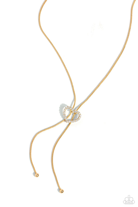 Paparazzi Accessories Tempting Tassel - Gold A dainty white rhinestone-encrusted heart silhouette slides along dainty strands of glistening gold snake chain for a timeless, refined tassel. Features a bolo closure. Sold as one individual necklace. Includes