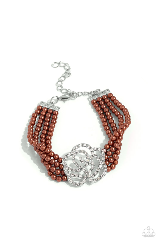 Paparazzi Accessories Regal Rose - Brown Held together by dainty silver plates, four strands of classic brown pearls are threaded around the wrist. Encrusted in glassy white rhinestones, a glitzy silver rose blooms at the center of the wrist for a fierce