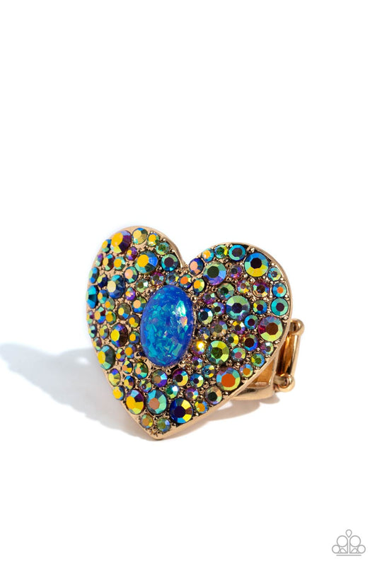Paparazzi Accessories Bejeweled Beau - Blue Encrusted in brilliant multicolored and iridescent rhinestones, a glittery gold heart frame adorns the center of an airy gold band for a flirtatious finish. Featuring iridescent flecks, an opalescent blue oval b