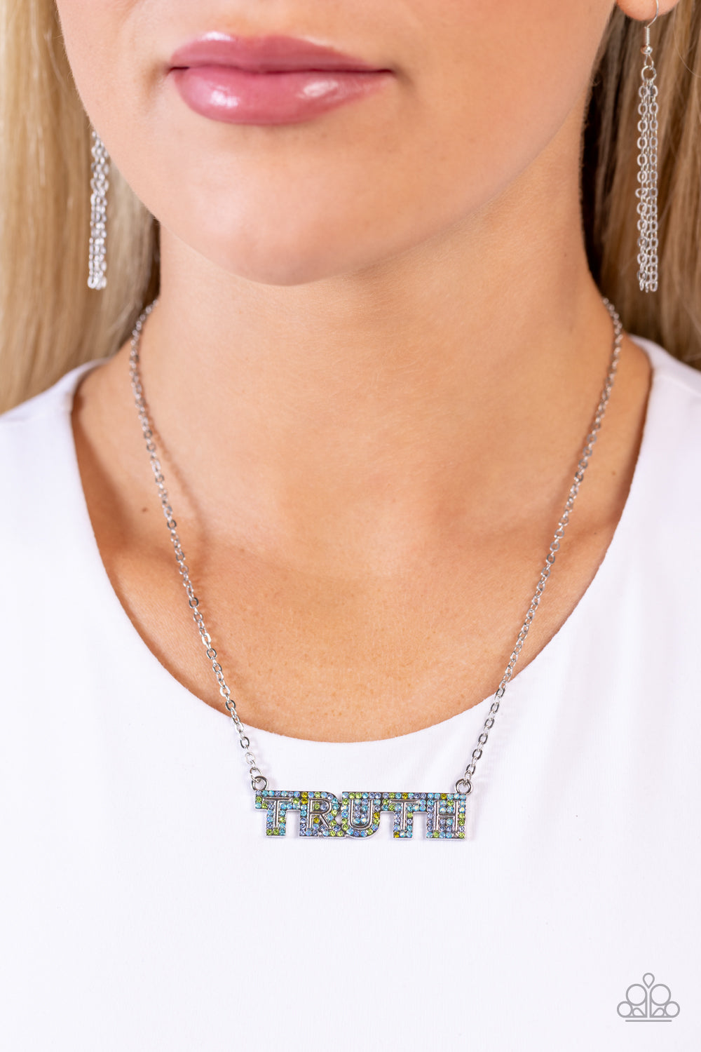 Paparazzi Accessories Truth Trinket - Blue Encrusted in glassy olive, Montana, aquamarine, and blue iridescent rhinestones, the silver word "TRUTH" connects to a dainty silver chain, creating an inspirational pendant below the collar. Features an adjustab