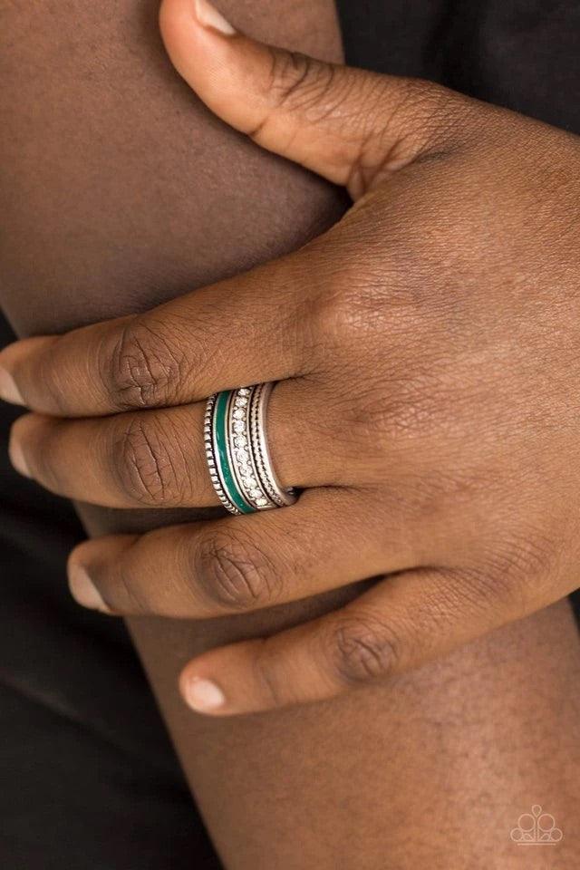 Paparazzi Accessories Rich Rogue - Green Tinted in the rich shade of Quetzal Green, a strip of color runs along the bottom of a row of glassy white rhinestones. Infused with silver textures, the mismatched details coalesce into one thick band across the f