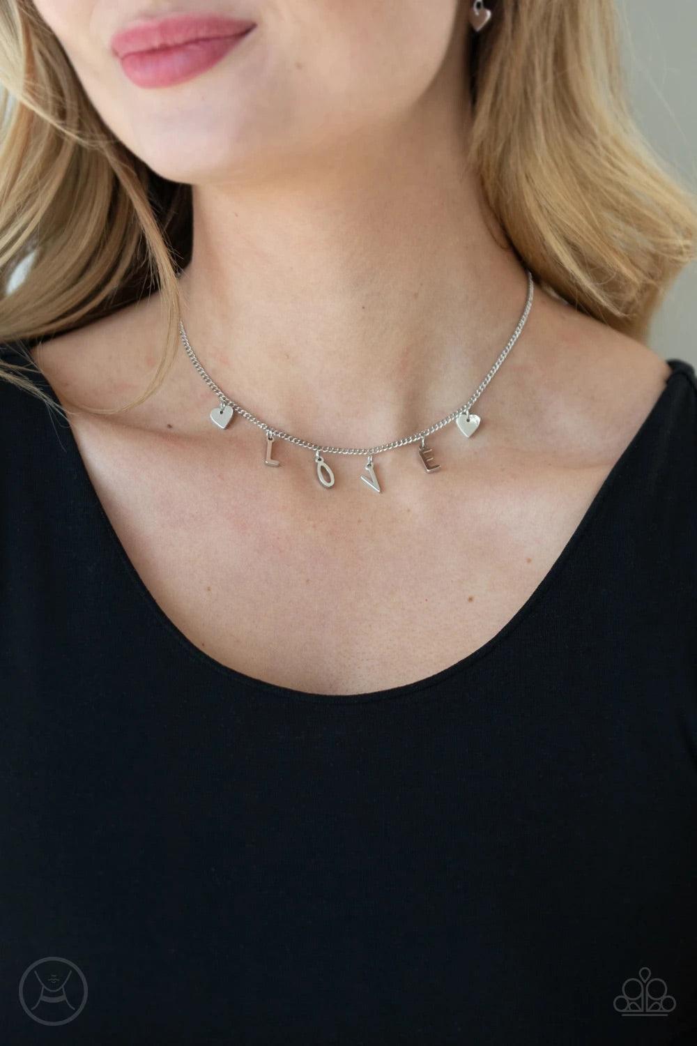 Paparazzi Accessories Love Conquers All - Silver Nestled between a pair of dainty silver hearts, dangling silver letter charms spell out the word, "LOVE," creating a flirty fringe around the neck. Features an adjustable clasp closure. Sold as one individu