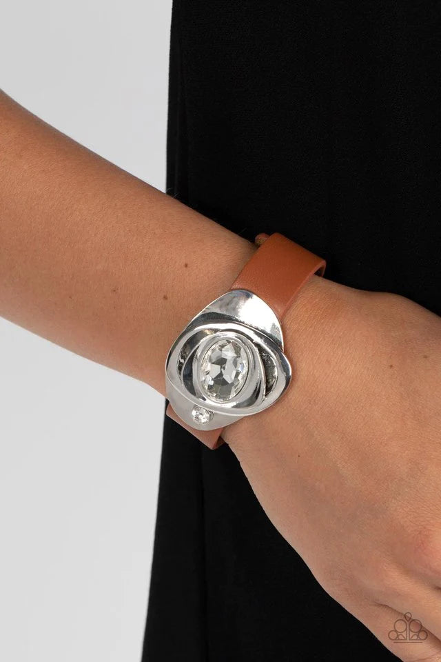 Paparazzi Accessories Pasadena Prairies - Brown Embellished with an oversized white oval gem, asymmetrical silver frames haphazardly stack into an abstract floral-inspired centerpiece. A smaller white rhinestone attaches the metallic structure to a band o