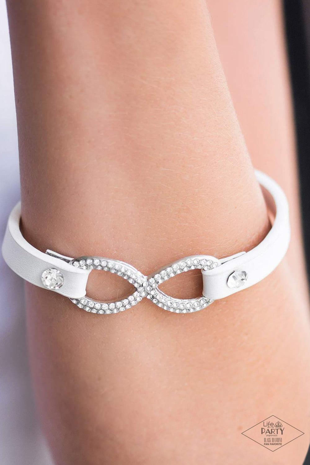 Paparazzi Accessories Innocent Till Proven GLITZY - White A skinny strip of white leather attaches to a silver infinity symbol encrusted in glittery rhinestones. Flanked by two dazzling solitaire rhinestones, the glitzy design creates an incandescent cent