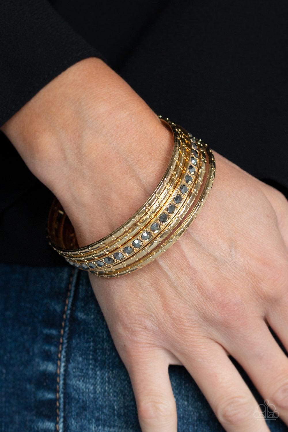 Paparazzi Accessories Glitzy Grunge - Gold A single hematite rhinestone encrusted bangle joins four textured gold bangles, creating an edgy stack of shimmer across the wrist. Jewelry