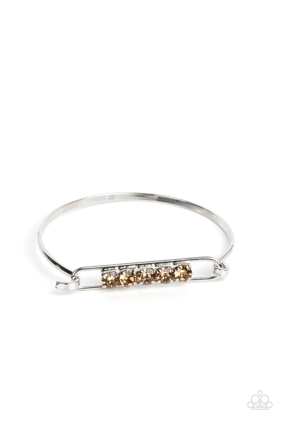 Paparazzi Accessories In CHARM’S Way - Brown Encased in silver square fittings, a row of golden topaz rhinestones are fitted in place along an airy silver frame that hinges to the center of a bangle-like bracelet for a timeless finish. Features a hinged c