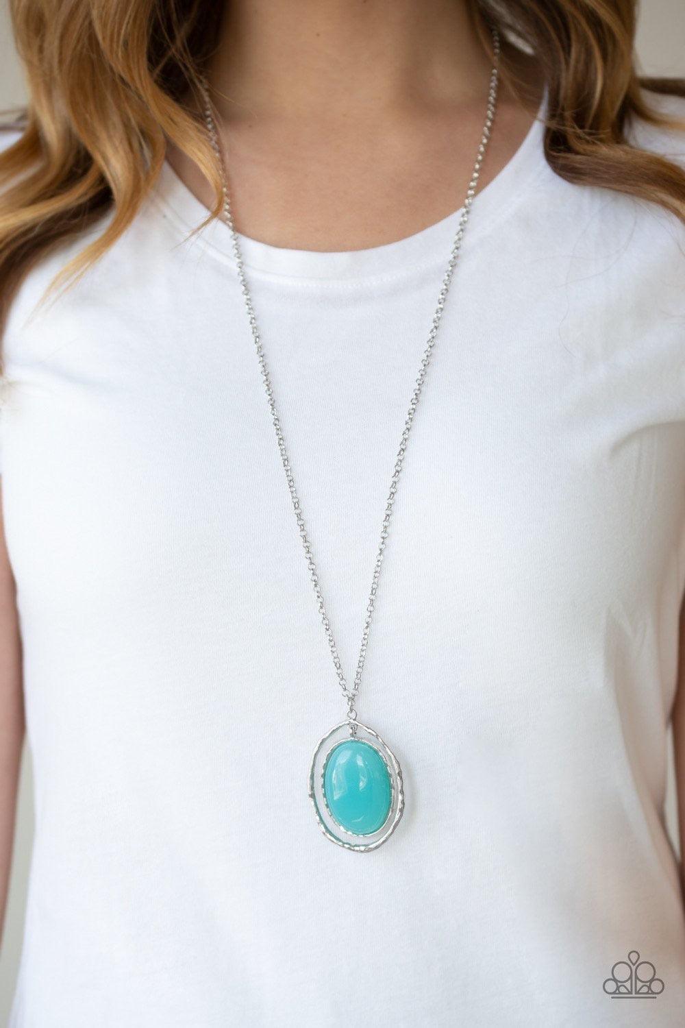 Paparazzi Accessories Harbor Harmony - Blue A dewy blue bead is pressed into the center of a stacked silver frame radiating with shimmery hammered textures. The oversized pendant swings from the bottom of a lengthened silver chain, adding a whimsical pop