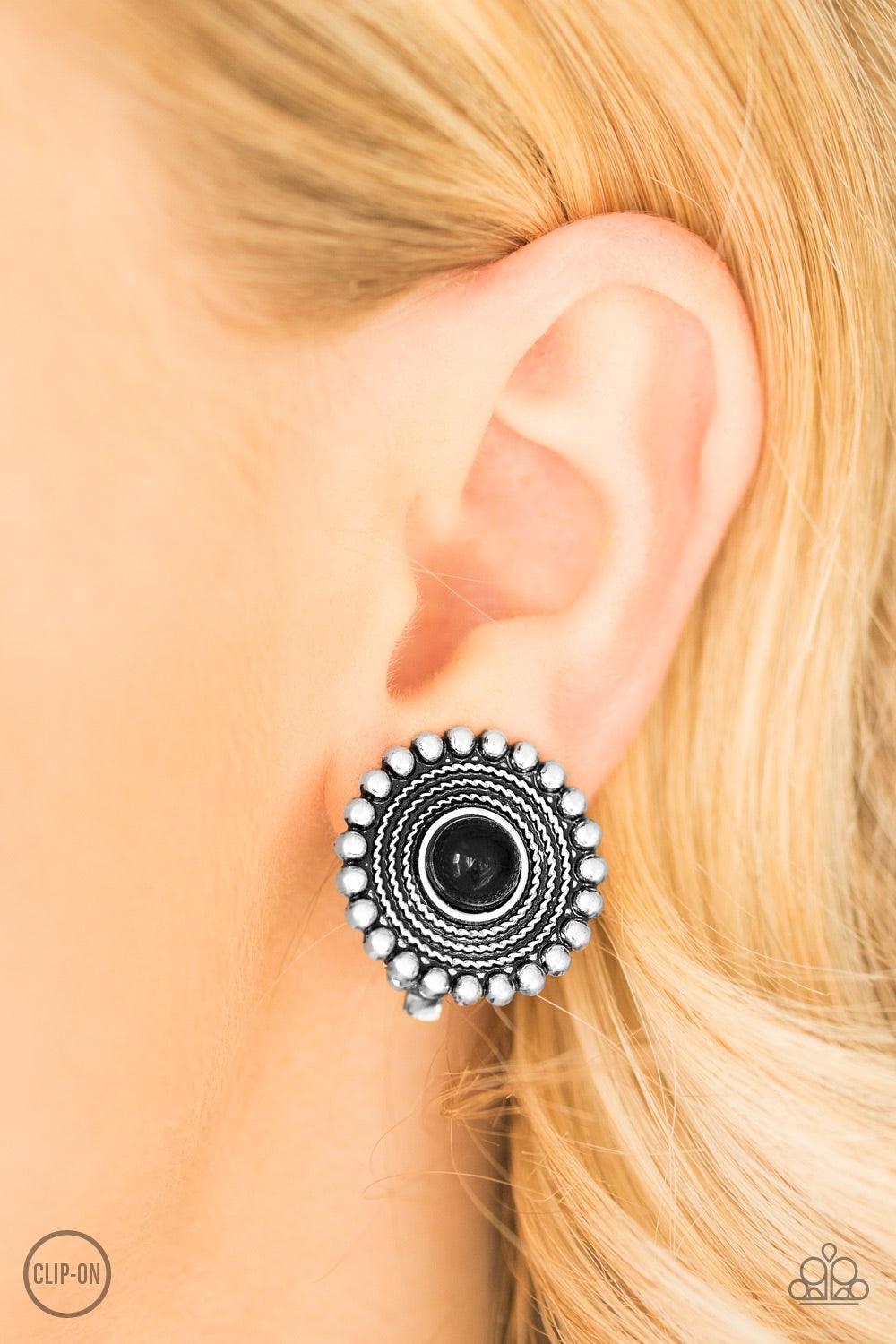 Paparazzi Accessories WHEELing And Able - Black *Clip-On A shiny black bead is pressed into the center of a silver studded frame radiating with shimmery texture for a tribal inspired look. Earring attaches to a standard clip-on fitting. Jewelry
