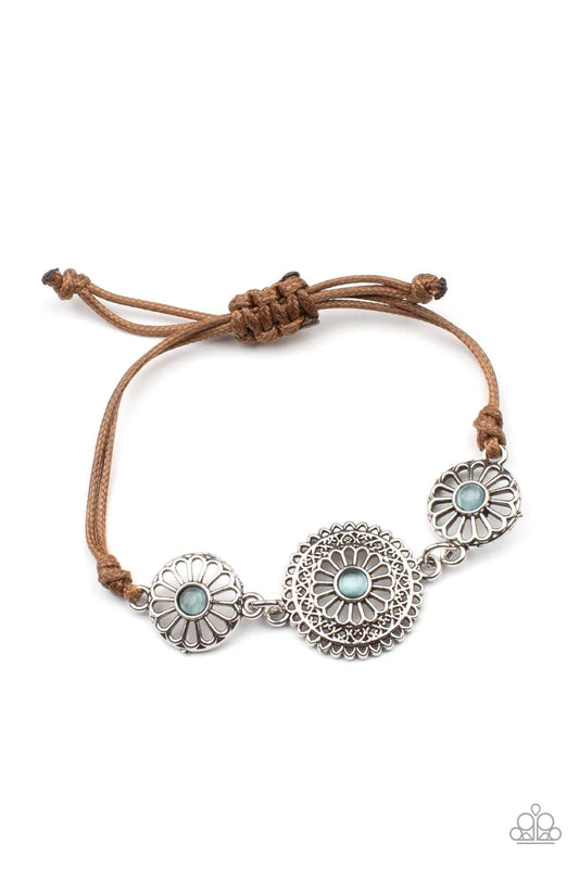 Paparazzi Accessories Bohemian Botany - Blue Dotted with dainty blue cat's eye stone centers, an airy trio of ornate floral frames delicately link across the wrist. The whimsy centerpiece is knotted in place around the wrist with shiny brown cording for a