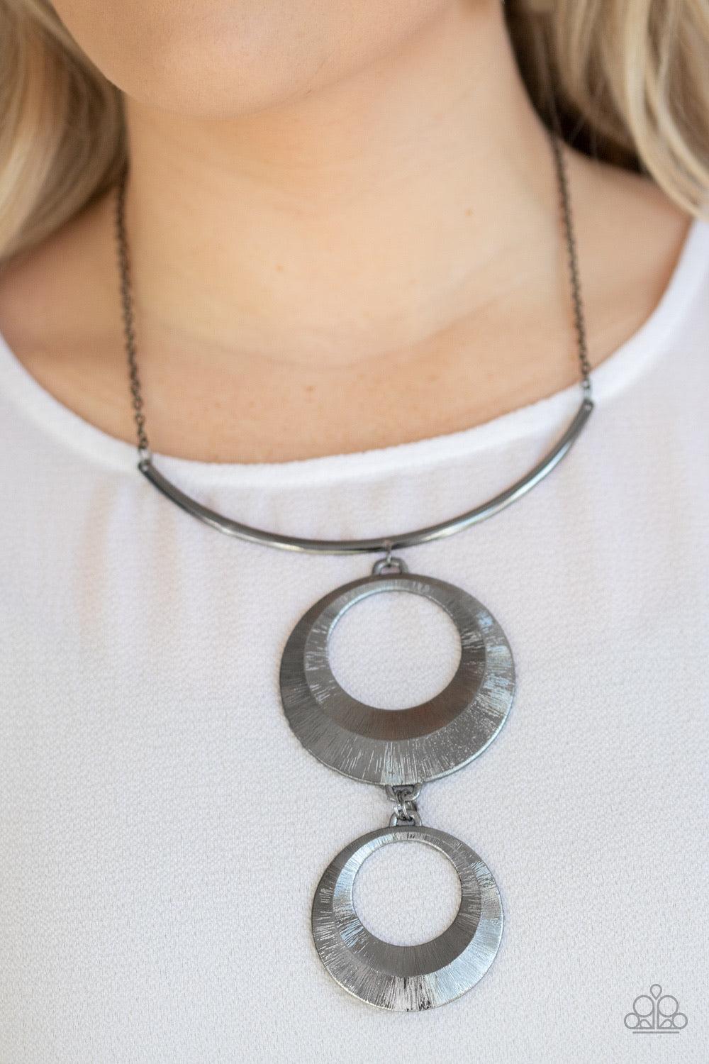 Paparazzi Accessories Egyptian Eclipse - Black Featuring a blinding scratch finish, two beveled gunmetal circular frames swing from the bottom of a bowing gunmetal rod, creating an edgy stacked pendant down the chest. Features an adjustable clasp closure.