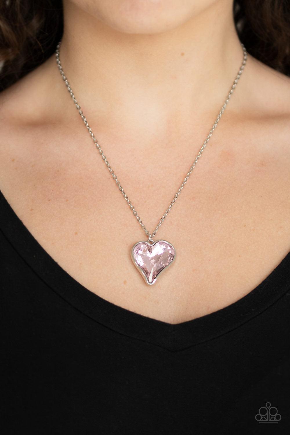Paparazzi Accessories Heart Flutter - Pink Chiseled into a charming heart, an oversized pink rhinestone gem is nestled inside a sleek silver frame, creating a flirtatious pendant below the collar. Features an adjustable clasp closure. Jewelry