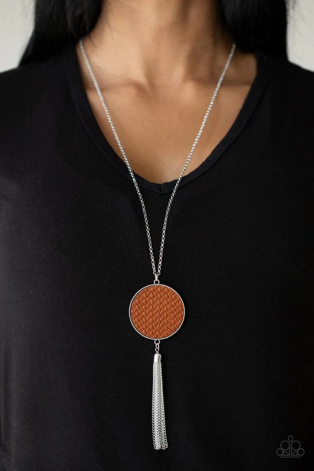 Paparazzi Accessories Wondrously Woven - Brown Featuring a faux woven finish, a shiny piece of Adobe leather is pressed into a studded circular frame at the bottom of a lengthened silver chain. Capped in a frame, a silver chain tassel streams out from the