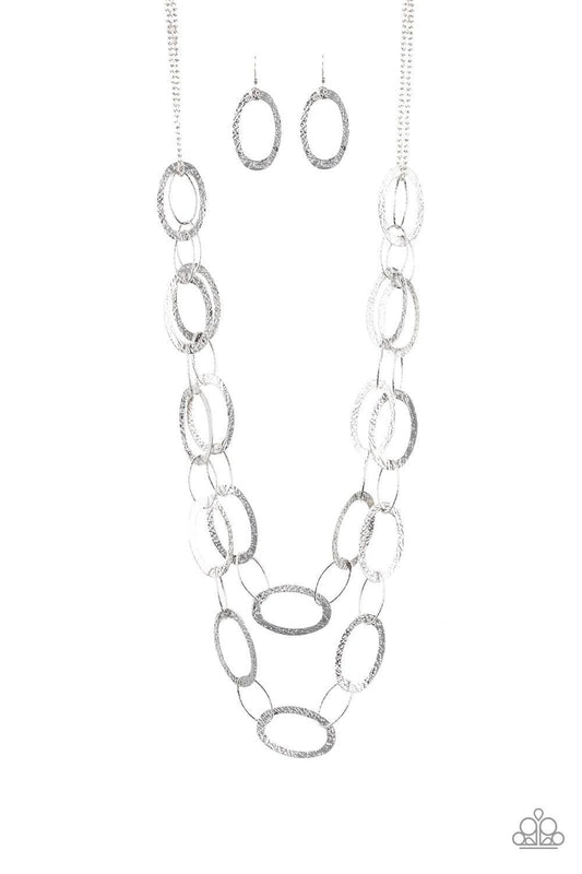 Paparazzi Accessories Glimmer Goals - Silver Delicately hammered in shimmery textures, two rows of glistening silver hoops layer down the chest for a sleek look. Features an adjustable clasp closure. Sold as one individual necklace. Includes one pair of m