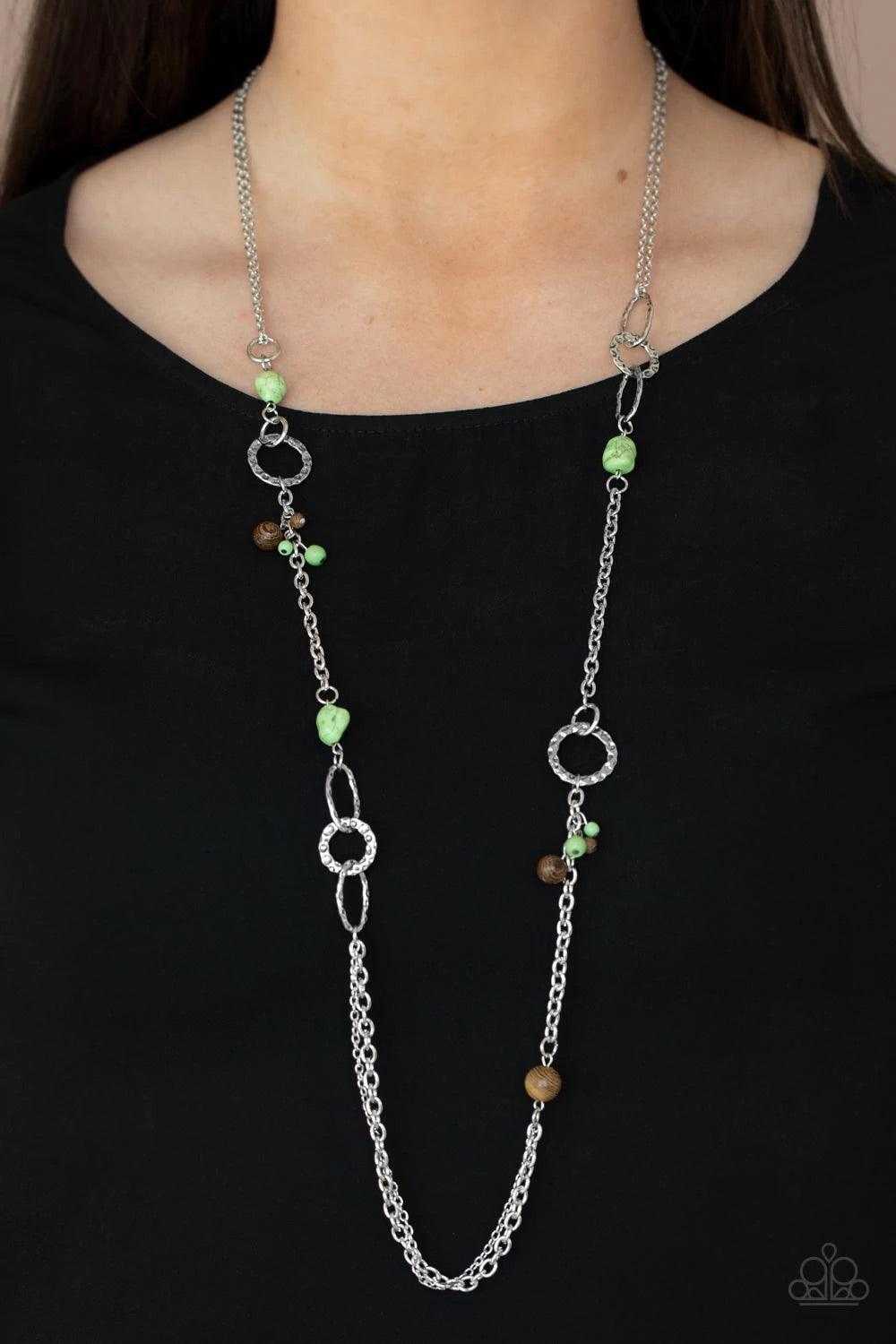 Paparazzi Accessories Sandstone Safari - Green A mismatched collection of brown wooden beads, green pebbles, hammered silver ovals, and dainty green stone beads haphazardly adorn sections of silver chain across the chest, creating an earthy seasonal flair
