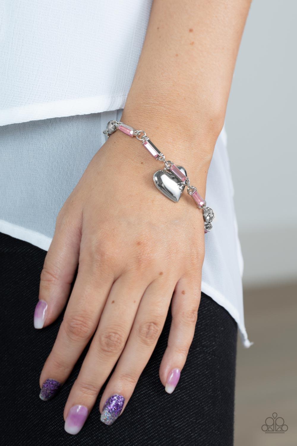 Paparazzi Accessories Sweetheart Secrets - Pink Encased in sleek silver fittings, classic white rhinestones and emerald cut pink rhinestones delicately link into a sparkly chain around the wrist. A shiny silver heart charm swings from the glittery compila
