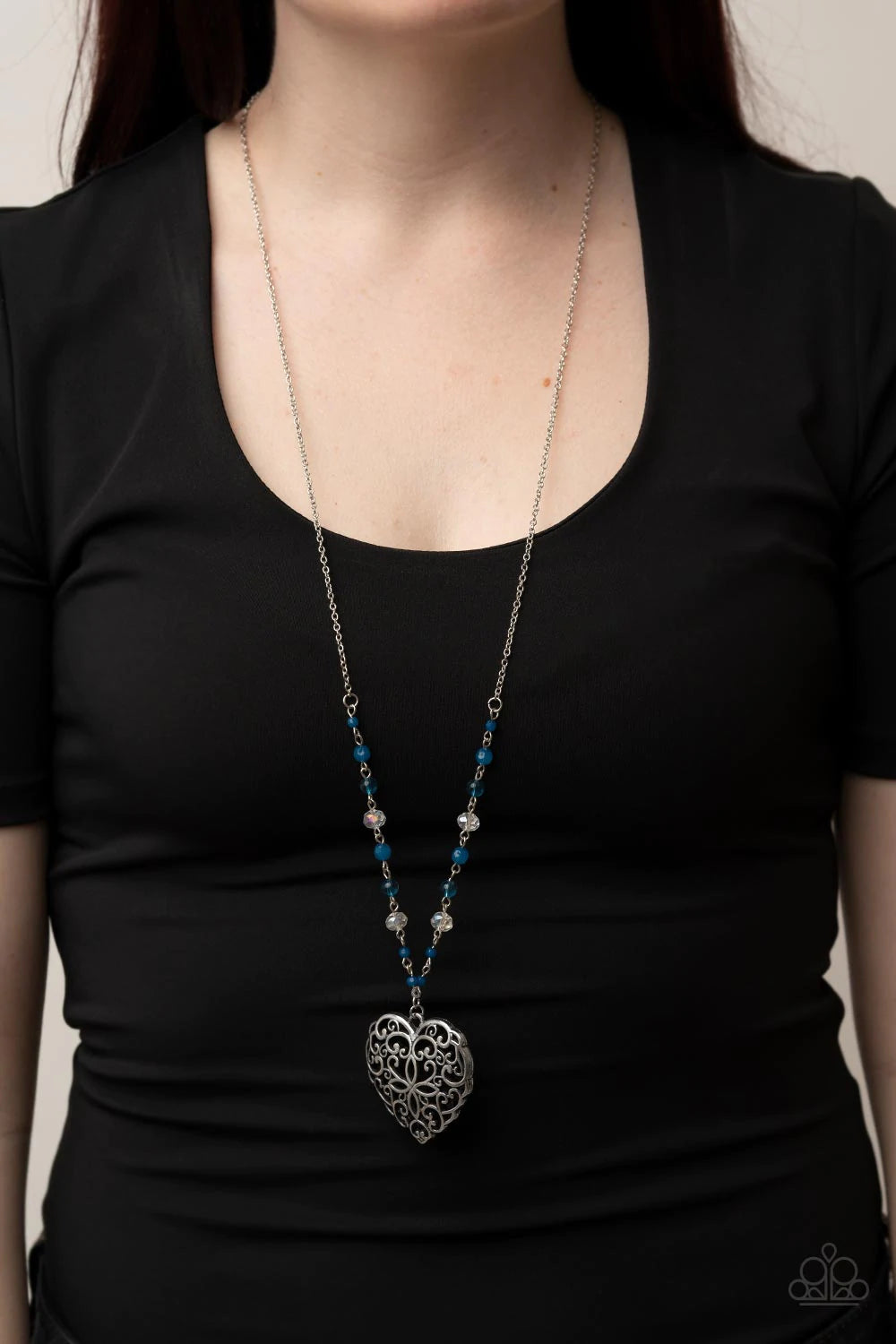Paparazzi Accessories Doting Devotion - Blue Featuring opaque and glassy crystal-like finishes, a dainty collection of Mykonos Blue and white beads gives way to an oversized filigree filled heart frame, creating an antiqued locket inspired pendant at the