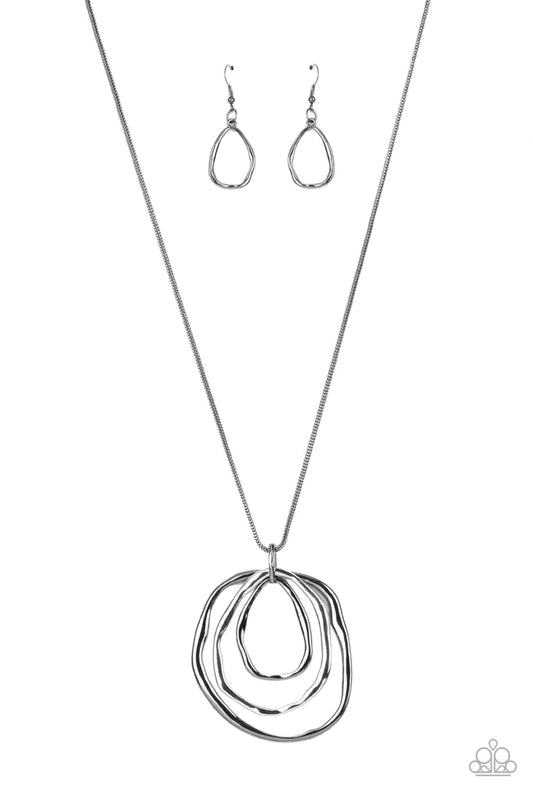 Paparazzi Accessories Revamped Relic - Black A trio of mismatched warped gunmetal and silver rings swing from the bottom of a glistening gunmetal chain, creating an asymmetrically stacked pendant. Features an adjustable clasp closure. Sold as one individu