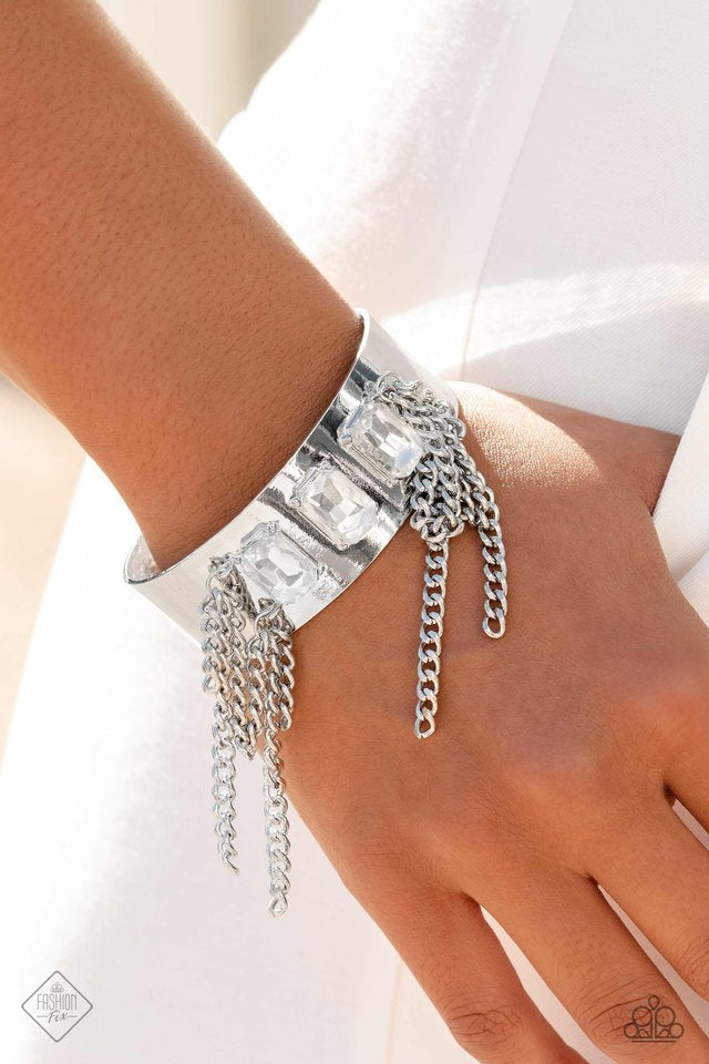 Paparazzi Accessories CHAIN Showers - White A thick, industrial silver cuff is topped by three brilliant white, emerald-cut gems. Strands of silver curb chain stream from each side of the trio of glitz, adding undeniable drama and eye-catching movement to