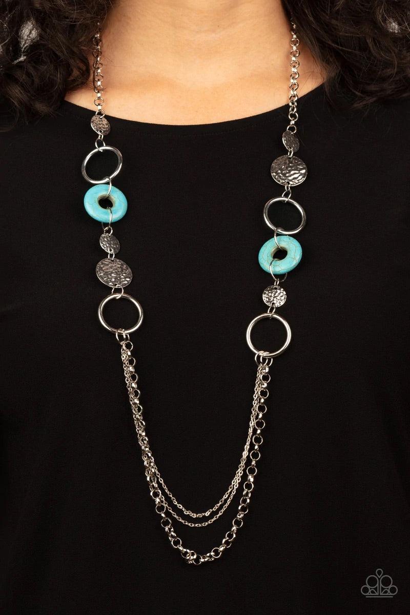 Paparazzi Accessories Grounded Glamour - Blue An earthy collection of hammered silver discs, turquoise stone accents, and bold silver hoops link with sections of chunky and mismatched silver chains across the chest, creating a seasonal display. Features a