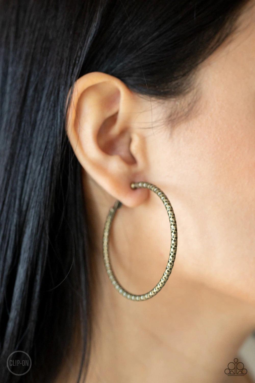 Paparazzi Accessories Subtly Sassy - Brass *Clip-On An oversized brass hoop featuring a porous-like texture sends off a subtle shimmer as it wraps around the ear. Earring attaches to a standard clip-on fitting. Hoop measures approximately 2" in diameter.