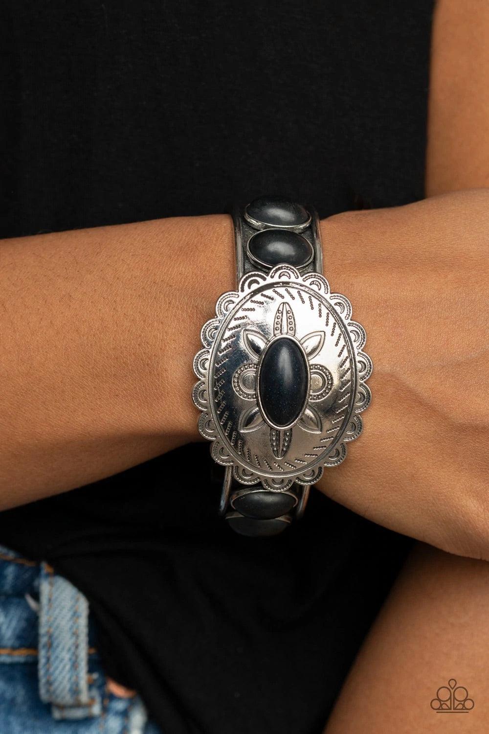 Paparazzi Accessories Canyon Heirloom - Black Dotted with an earthy black stone, a floral stamped scalloped silver frame sits atop a black stone studded silver cuff, creating a southwestern inspired buckle atop the wrist. Sold as one individual bracelet.