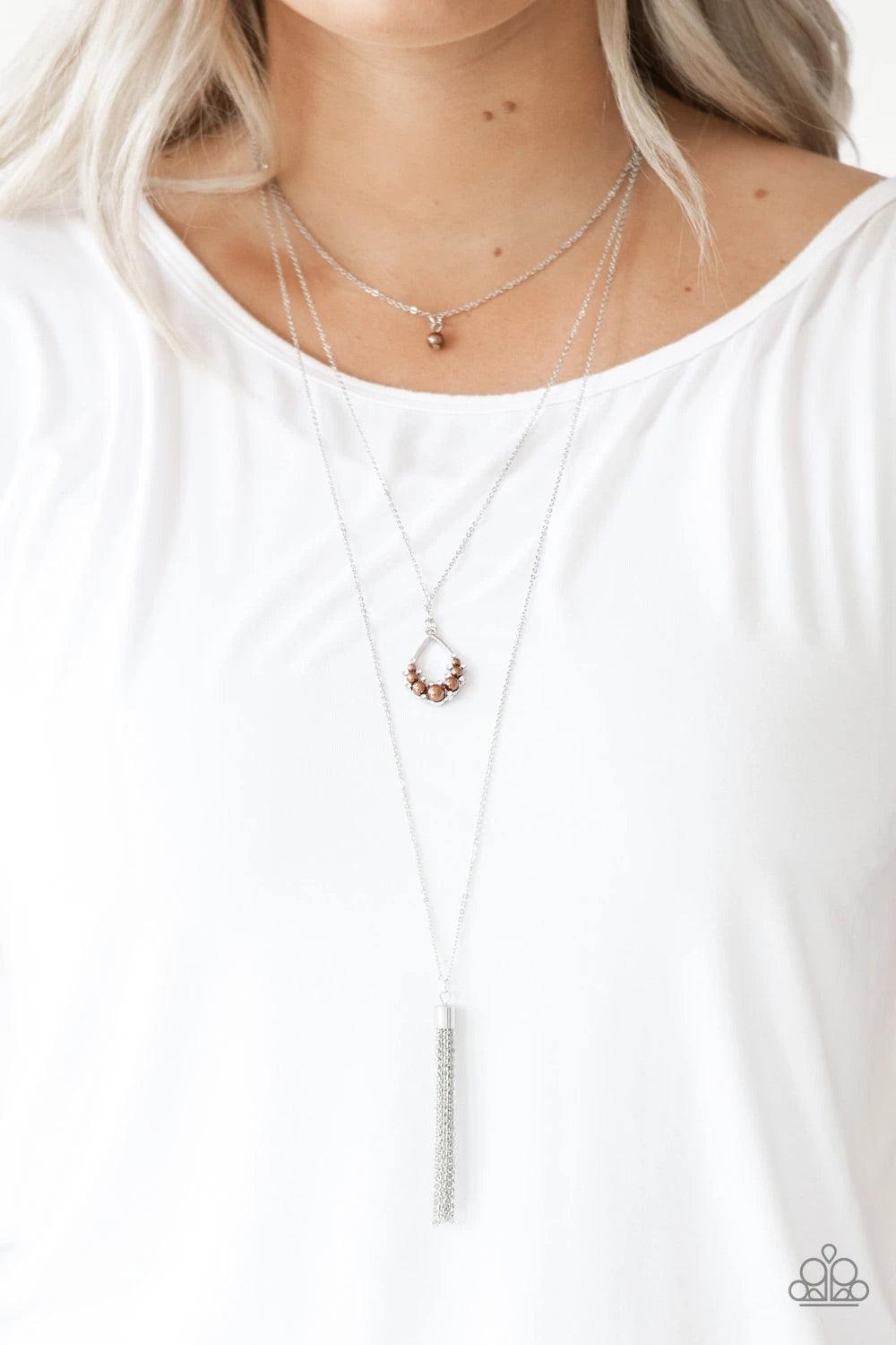 Paparazzi Accessories Be Fancy - Brown A solitaire brown pearl swings from the uppermost chain, giving way to a teardrop pendant and shimmery silver chain tassel. Dainty white rhinestones and brown pearls collect at the bottom of the centermost pendant fo
