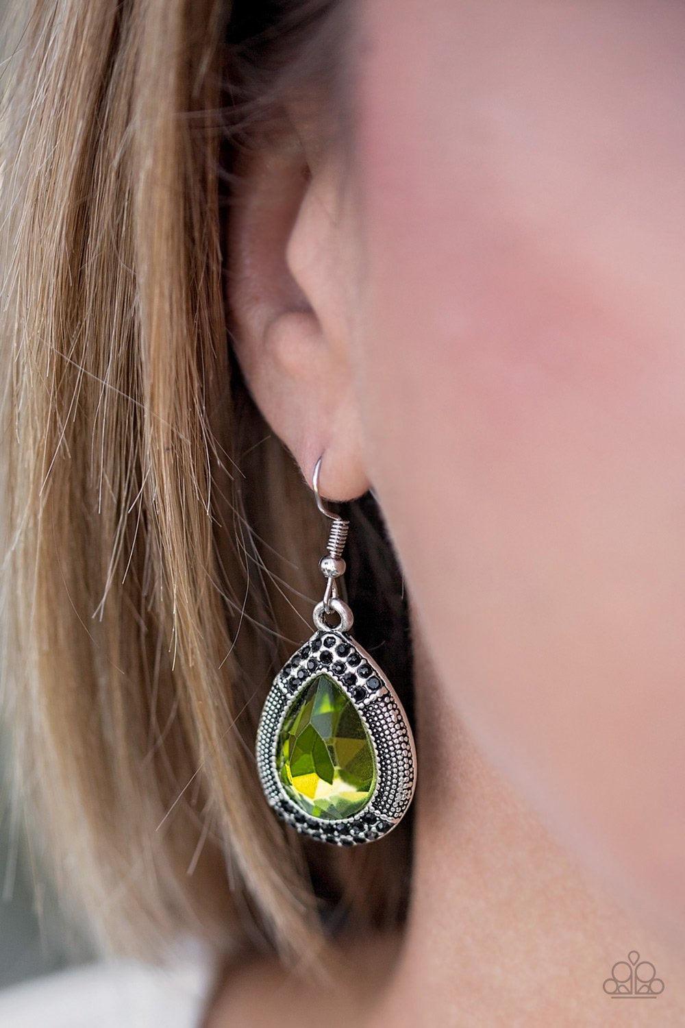 Paparazzi Accessories Grandmaster Shimmer - Green A faceted green teardrop gem is pressed into a shimmery silver frame radiating with studded details and glittery black rhinestones for a magnificent look. Earring attaches to a standard fishhook fitting. J