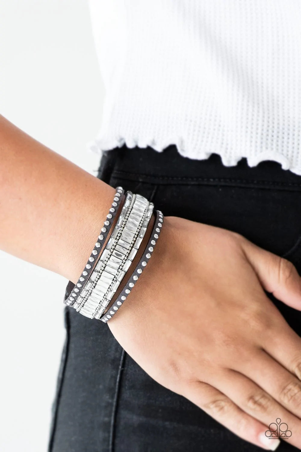 Paparazzi Accessories Rock Star Rocker - Silver Shiny silver studs, dainty silver ball chains, and edgy white emerald-cut rhinestones race along a spliced gray suede band for a rock star look. Features an adjustable snap closure. Sold as one individual br