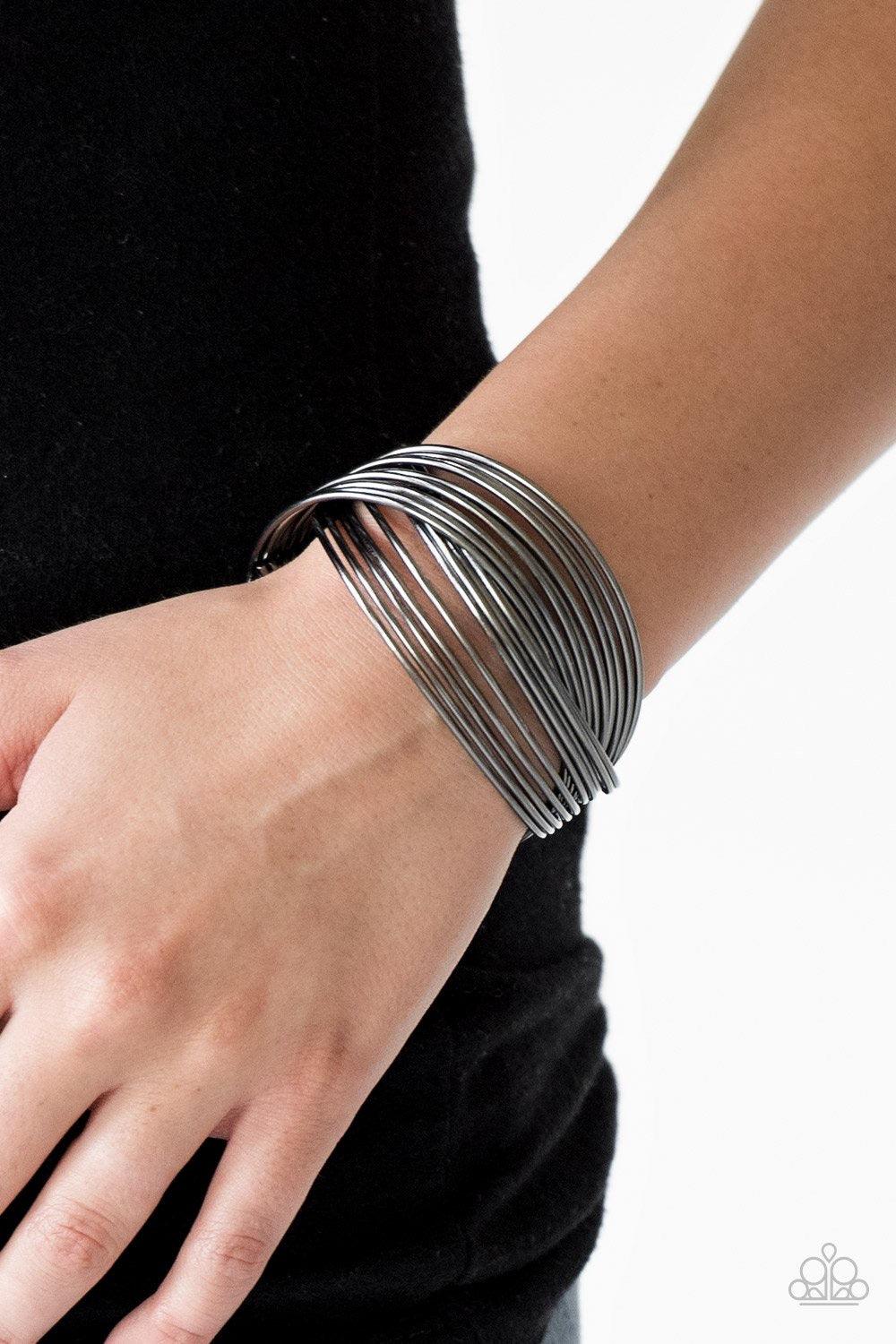 Paparazzi Accessories Urban Glam ~Black Threaded along two metallic rods, glistening gunmetal bars crisscross across the wrist, coalescing into a layered cuff.