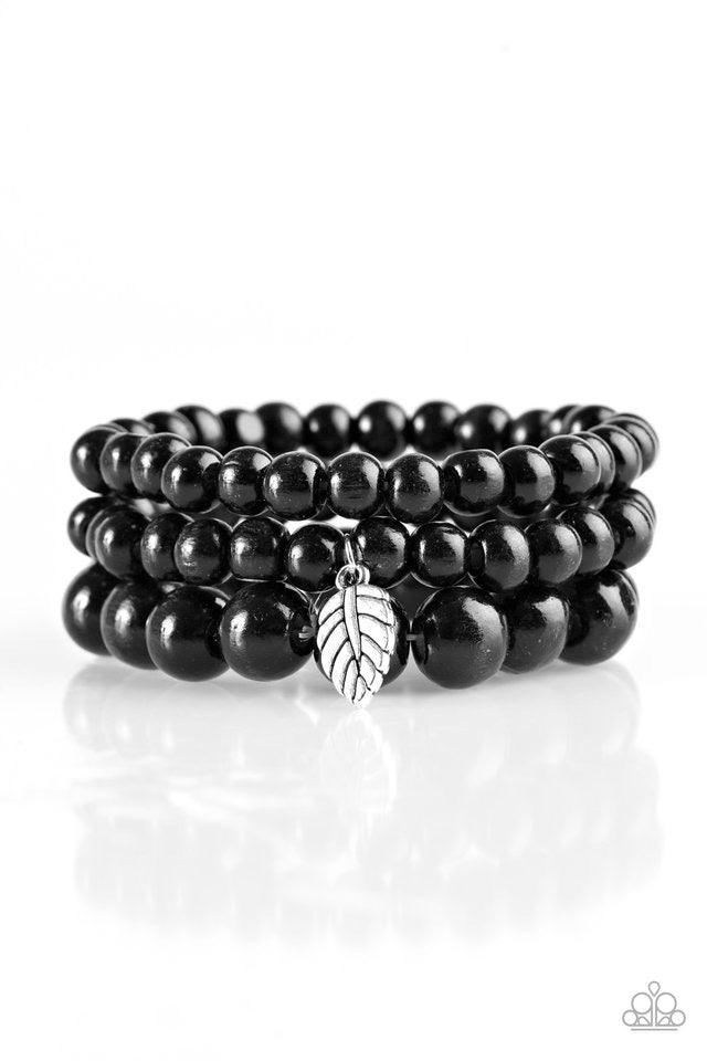 Paparazzi Accessories Out of the Woods - Black Painted in a neutral black finish, wooden beads are threaded along three elastic bands. A shimmery silver leaf charm swings from the wrist, adding a wanderlust finish to the seasonal look. Sold as one set of