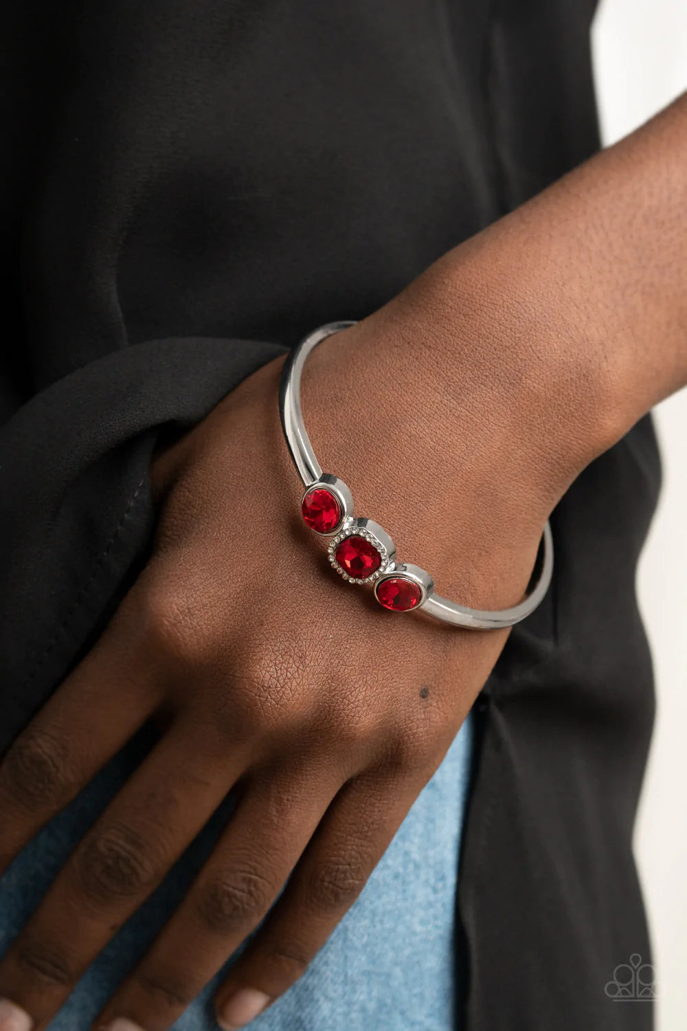 Paparazzi Accessories Royal Demands - Red The center of a thick silver bangle has been adorned with a trio of glittery red rhinestones, creating a sparkly centerpiece around the wrist. Featuring a regal cube cut, the centermost rhinestone is bordered in a